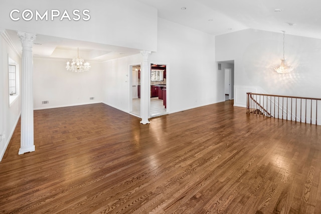 spare room featuring wood finished floors, decorative columns, baseboards, and an inviting chandelier