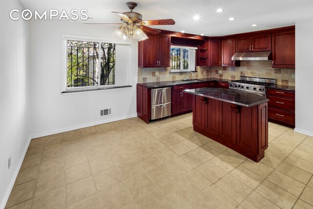 kitchen with reddish brown cabinets, under cabinet range hood, and gas stove