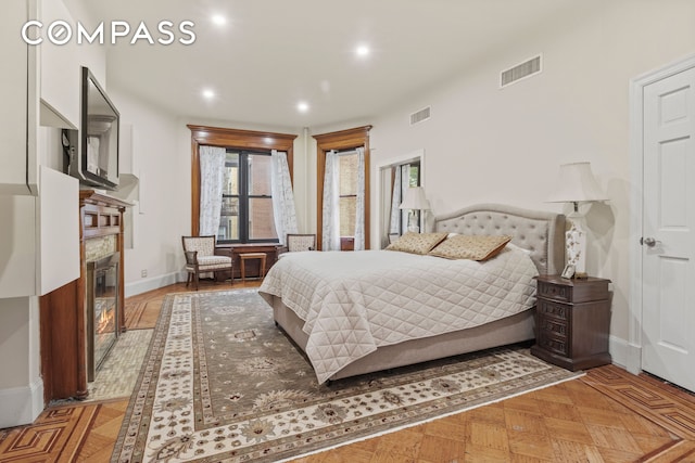 bedroom featuring a glass covered fireplace, visible vents, baseboards, and recessed lighting