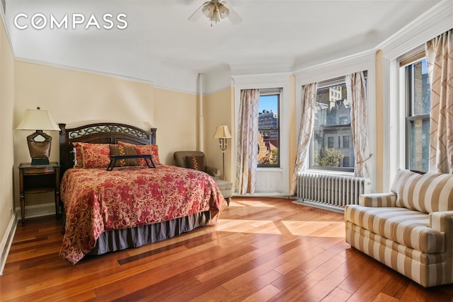 bedroom with radiator, multiple windows, and wood finished floors