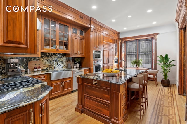 kitchen featuring glass insert cabinets, stainless steel dishwasher, light wood-type flooring, dark stone counters, and a center island with sink