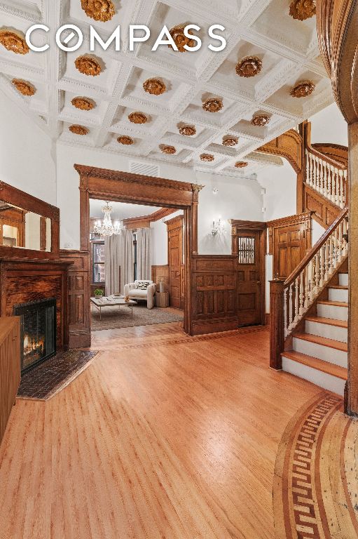 unfurnished living room with beam ceiling, coffered ceiling, a chandelier, and light wood-type flooring