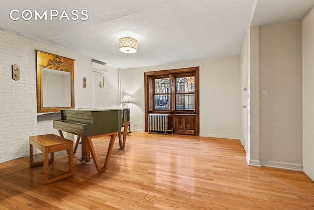 sitting room with light wood-style floors, brick wall, a wall mounted air conditioner, and radiator heating unit