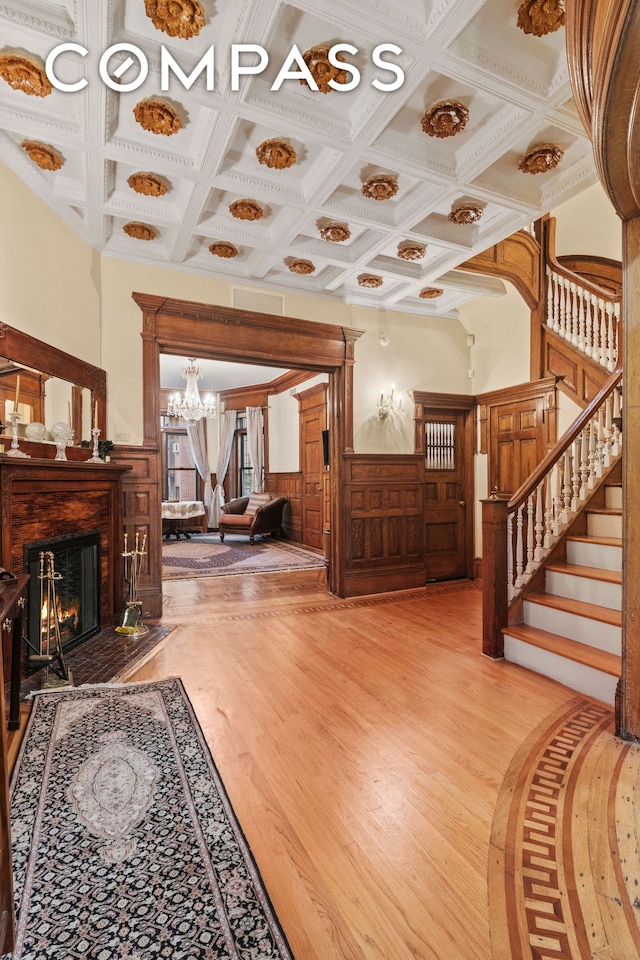 foyer with a warm lit fireplace, stairway, wood finished floors, and wainscoting