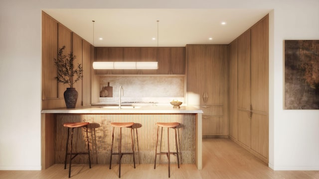 kitchen with brown cabinetry, a kitchen breakfast bar, light countertops, light wood-style floors, and a sink