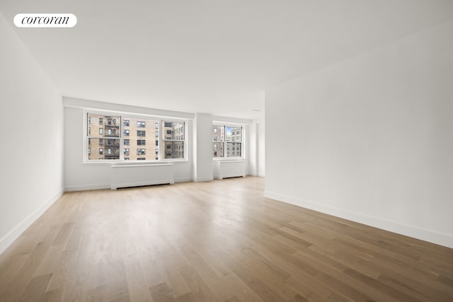 spare room featuring radiator heating unit, wood finished floors, visible vents, and baseboards