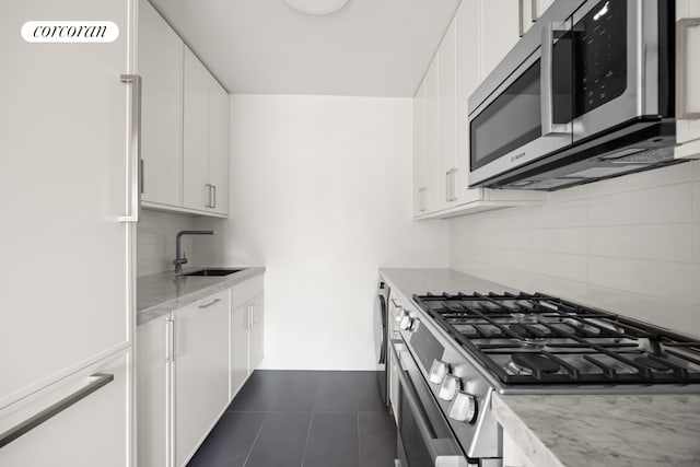 kitchen with dark tile patterned flooring, a sink, white cabinets, appliances with stainless steel finishes, and backsplash