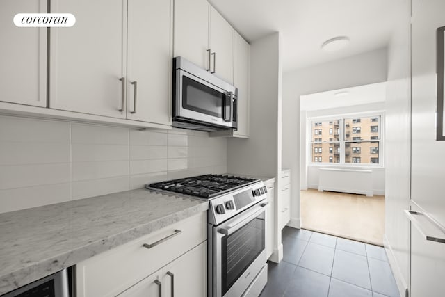 55 E 87th St Unit 14E, New York City, NY 10128 - kitchen with stainless steel appliances, tasteful backsplash, tile patterned floors, light stone countertops, and white cabinetry