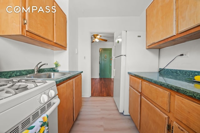 kitchen with dark countertops, white appliances, a ceiling fan, and a sink