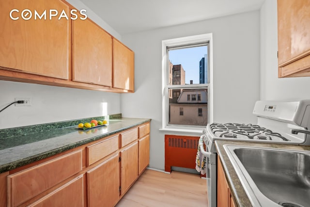 kitchen featuring white gas stove, light wood-style flooring, radiator, and dark countertops