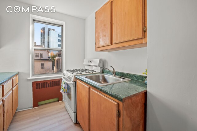 kitchen with light wood finished floors, white gas range, dark countertops, radiator, and a sink