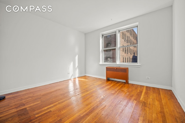 unfurnished room featuring radiator, baseboards, and hardwood / wood-style flooring