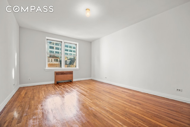 empty room with baseboards, hardwood / wood-style floors, and radiator