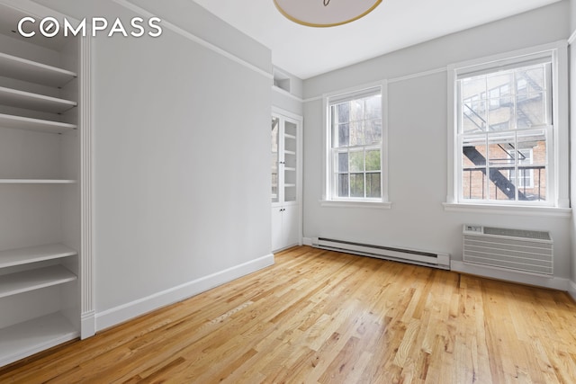 interior space featuring baseboards, baseboard heating, an AC wall unit, and wood finished floors