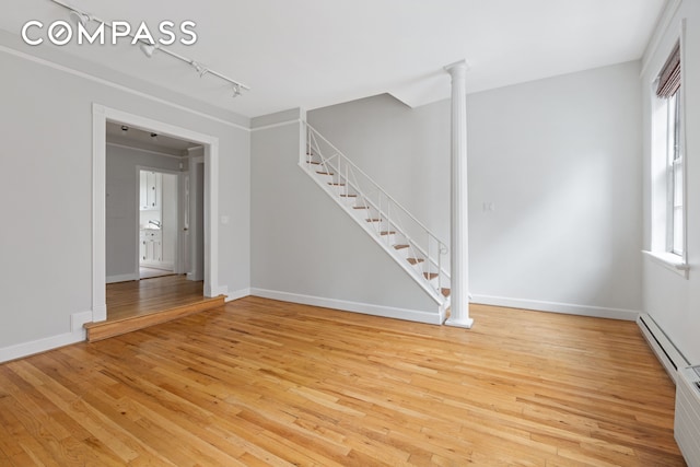 unfurnished room with decorative columns, light wood-style flooring, track lighting, baseboards, and stairs