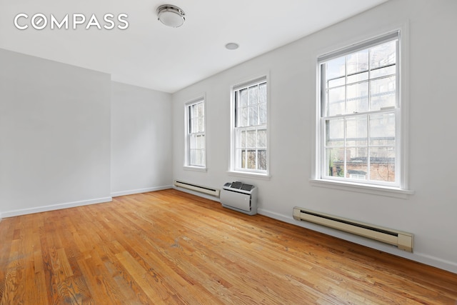 empty room with light wood-type flooring, a baseboard radiator, a baseboard heating unit, and a wealth of natural light