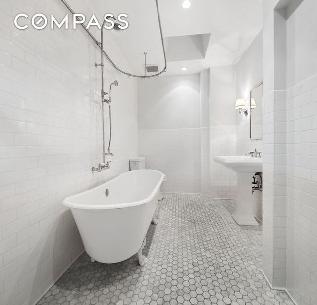 bathroom with a sink, visible vents, tile walls, a freestanding bath, and tile patterned floors