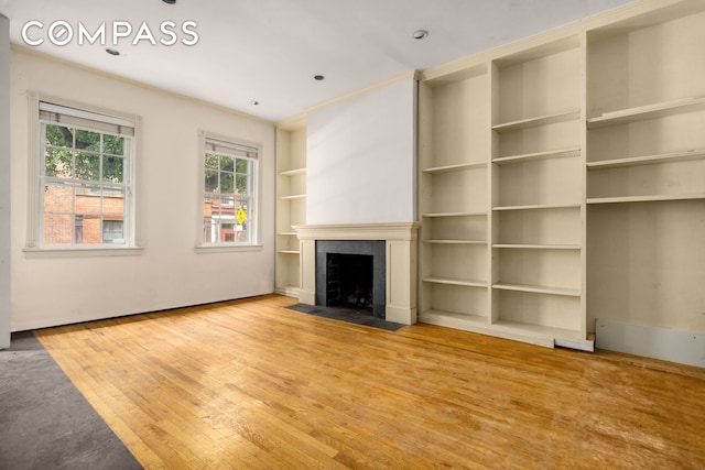 unfurnished living room featuring built in shelves, crown molding, a tiled fireplace, and wood finished floors