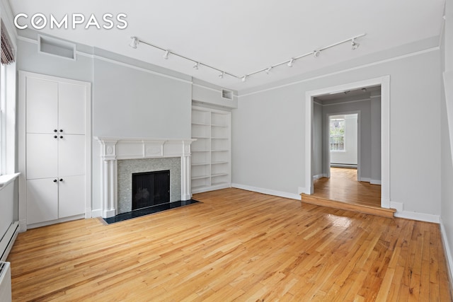 unfurnished living room with a fireplace with flush hearth, a baseboard heating unit, light wood-style flooring, and baseboards