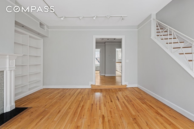 unfurnished living room featuring light wood-style flooring, baseboards, stairs, built in features, and track lighting