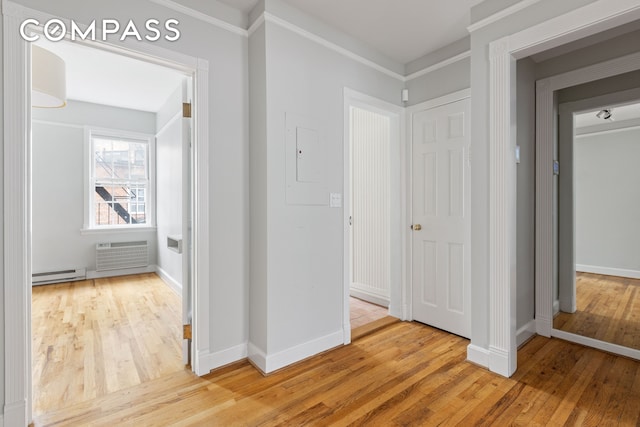 hallway with a wall unit AC, a baseboard heating unit, baseboards, ornamental molding, and light wood finished floors