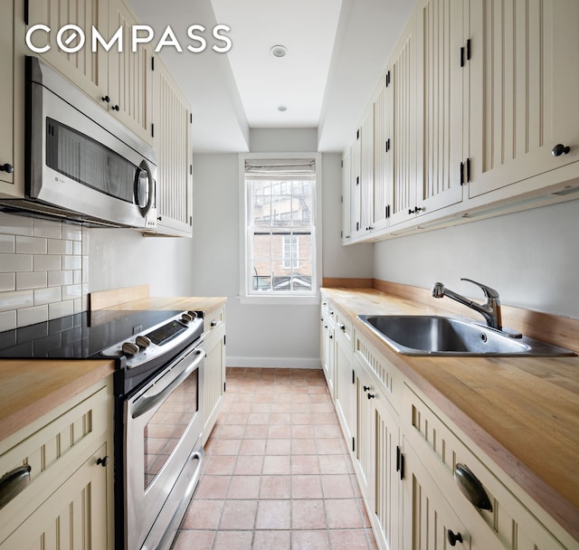 10 Bedford St, New York City, NY 10014 - kitchen with appliances with stainless steel finishes, butcher block counters, decorative backsplash, and light tile patterned floors