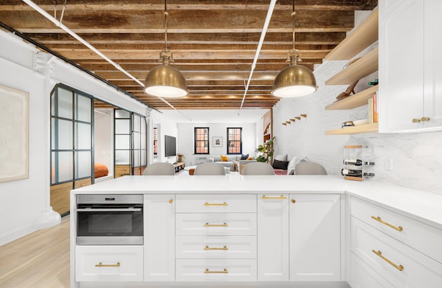 kitchen with light countertops, pendant lighting, oven, and white cabinetry