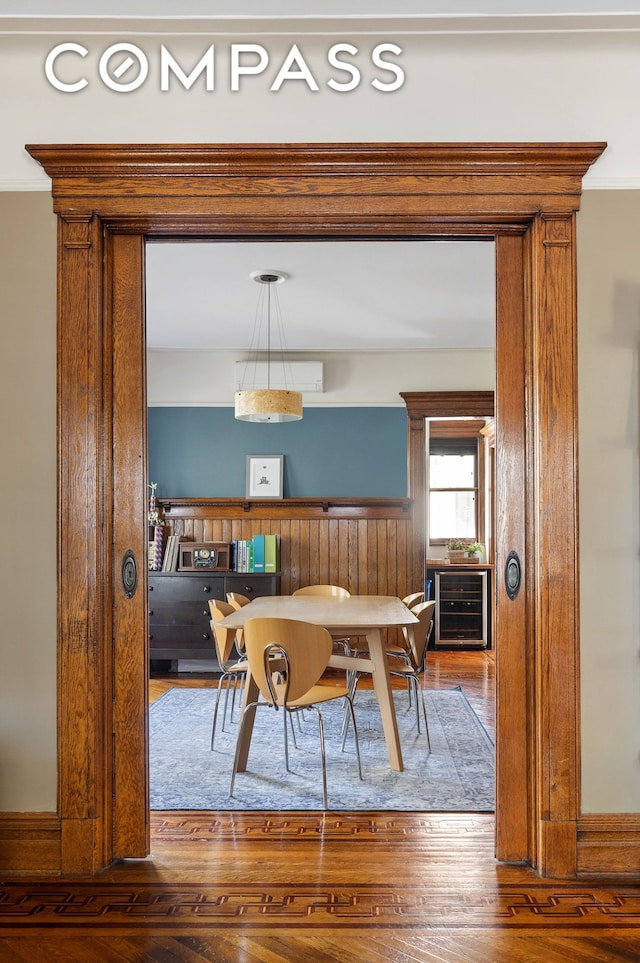 dining area featuring wine cooler, ornamental molding, and wood finished floors