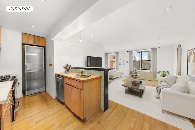 kitchen featuring a peninsula, appliances with stainless steel finishes, light wood finished floors, and open floor plan