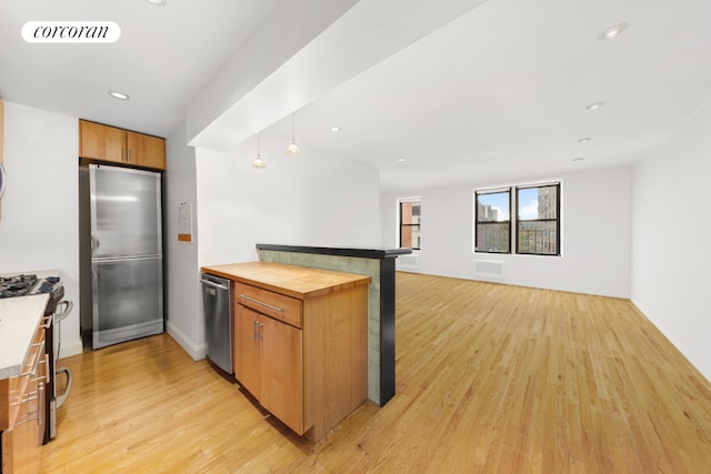 kitchen with appliances with stainless steel finishes, wood counters, pendant lighting, and light hardwood / wood-style floors