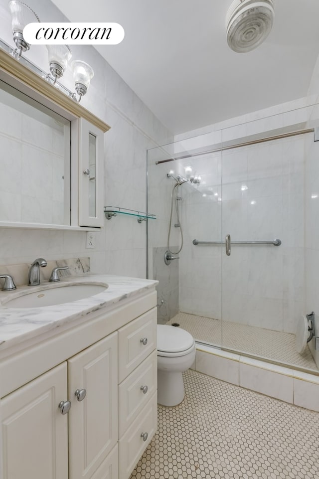 bathroom featuring tile walls, a shower stall, toilet, and vanity