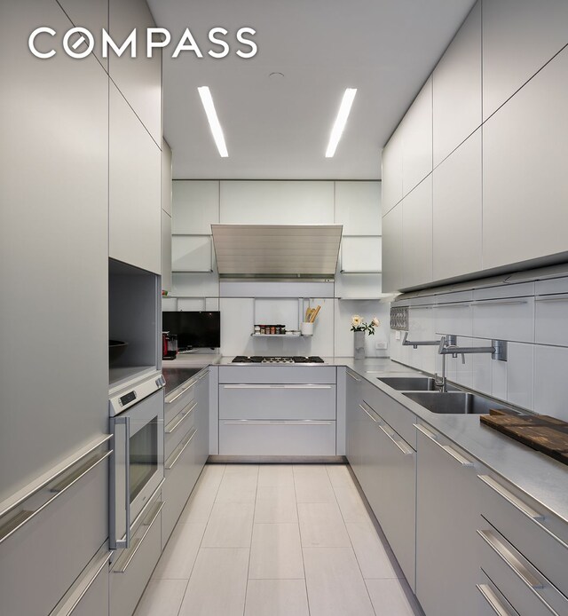 kitchen with a sink, decorative backsplash, white cabinetry, wall chimney exhaust hood, and modern cabinets