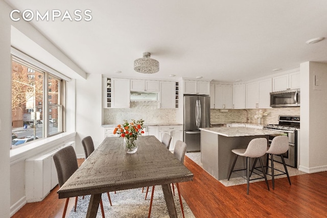 kitchen with dark wood-type flooring, a breakfast bar, white cabinetry, a center island, and appliances with stainless steel finishes