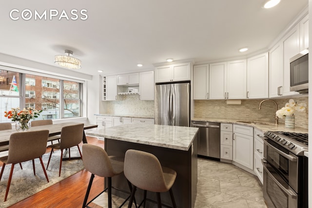 kitchen with stainless steel appliances, a kitchen island, a sink, white cabinets, and a kitchen bar