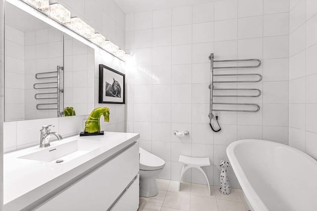 bathroom with tile patterned flooring, toilet, vanity, a freestanding tub, and tile walls