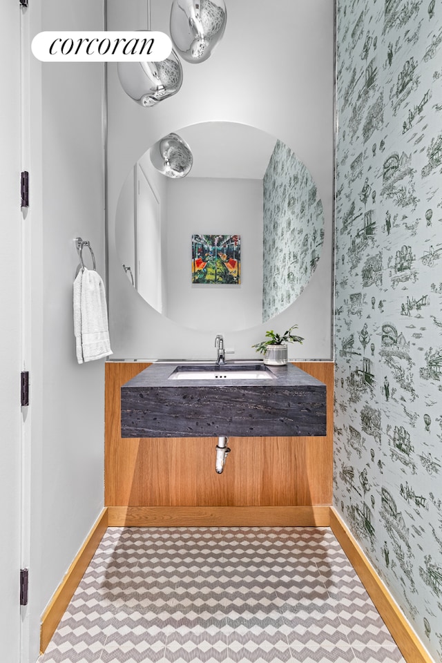 bathroom with a sink, baseboards, and wallpapered walls