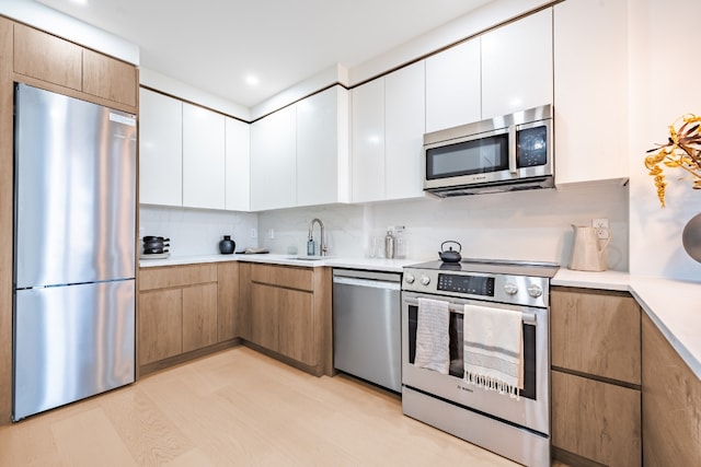 kitchen featuring white cabinets, appliances with stainless steel finishes, light hardwood / wood-style flooring, and sink