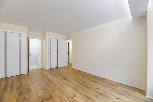 unfurnished bedroom with ensuite bathroom, two closets, and light wood finished floors