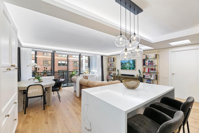 kitchen featuring white cabinetry, hanging light fixtures, light hardwood / wood-style flooring, and light stone countertops