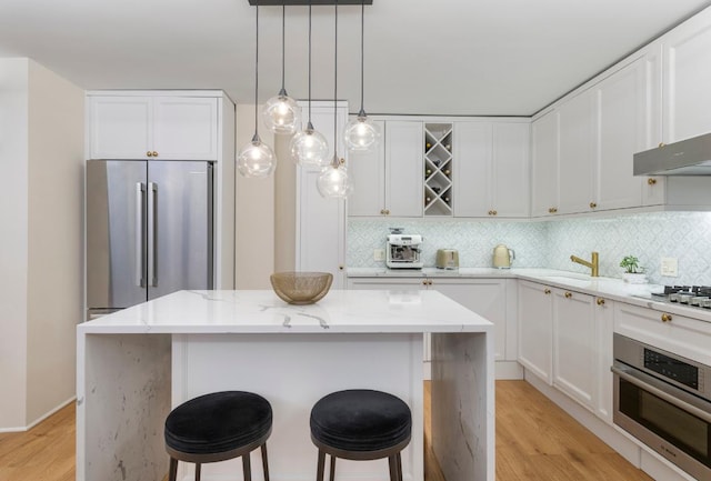 kitchen with stainless steel appliances, light stone countertops, a center island, and white cabinets