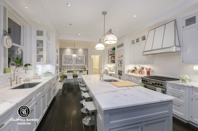 kitchen with a sink, custom range hood, white cabinets, crown molding, and recessed lighting