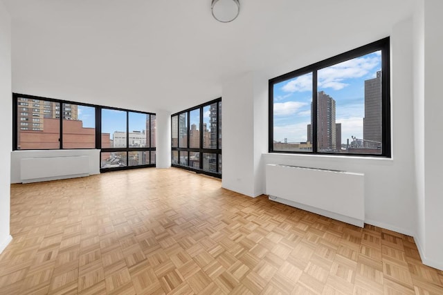 empty room with light parquet floors, a healthy amount of sunlight, and radiator heating unit