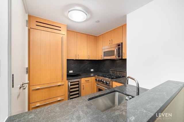 kitchen with beverage cooler, dark stone counters, appliances with stainless steel finishes, a sink, and backsplash