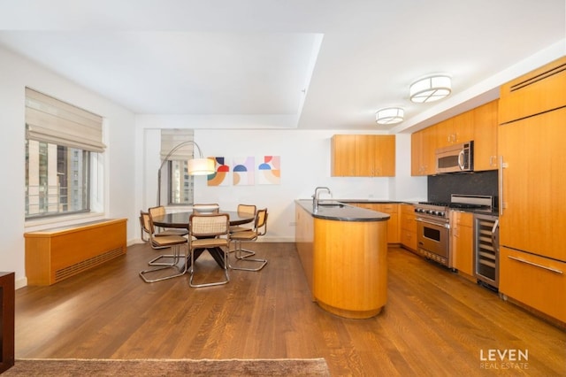 kitchen featuring sink, dark wood-type flooring, stainless steel appliances, tasteful backsplash, and beverage cooler