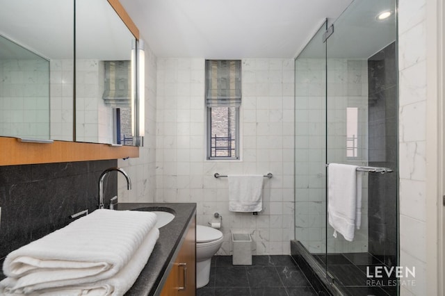 bathroom featuring tile patterned floors, toilet, a shower with shower door, tile walls, and vanity