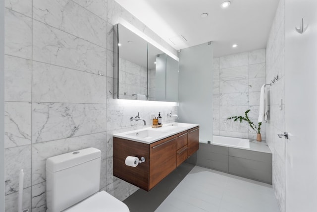 bathroom featuring a bathtub, a sink, toilet, and tile walls