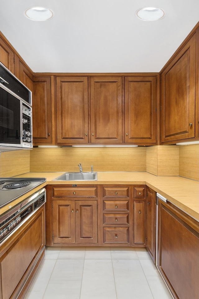 kitchen featuring a sink, stainless steel microwave, brown cabinets, and light countertops