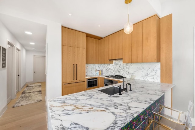 kitchen with decorative light fixtures, tasteful backsplash, modern cabinets, a sink, and light stone countertops