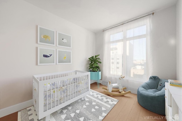 bedroom featuring a crib, multiple windows, baseboards, and wood finished floors