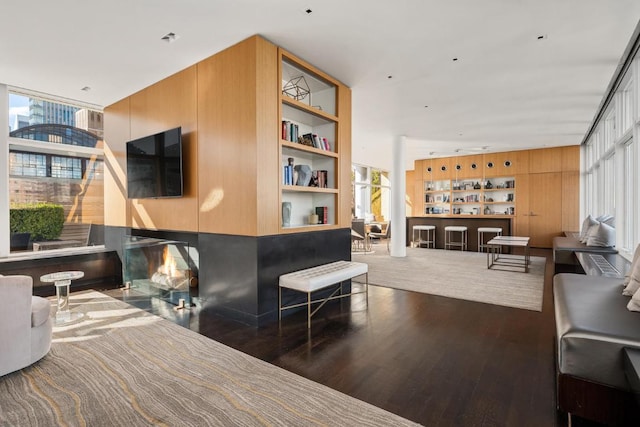 living room with built in shelves, wood walls, a healthy amount of sunlight, and hardwood / wood-style floors